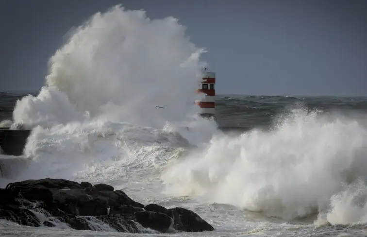 Onda alta a bater num rochedo que tem um farol vermelho.